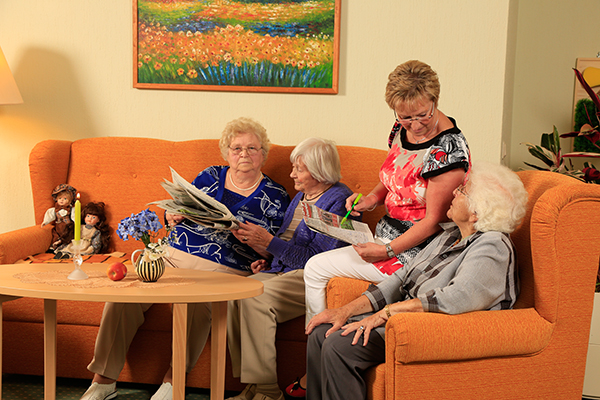 Seniorinnen mit Betreuungskraft am Tisch bei der Zeitungsschau